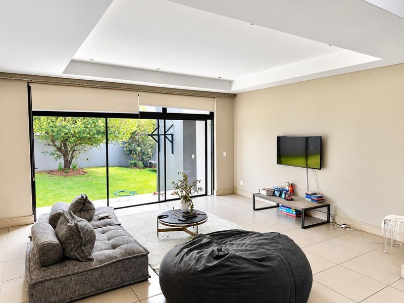 Spacious living room featuring large sliding glass doors that open to a private garden, complemented by a modern recessed ceiling and neutral tiled flooring.