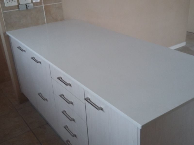 A clean, modern kitchen island featuring white cabinetry, ample drawer storage, and a smooth countertop, set against a tiled floor and backsplash.