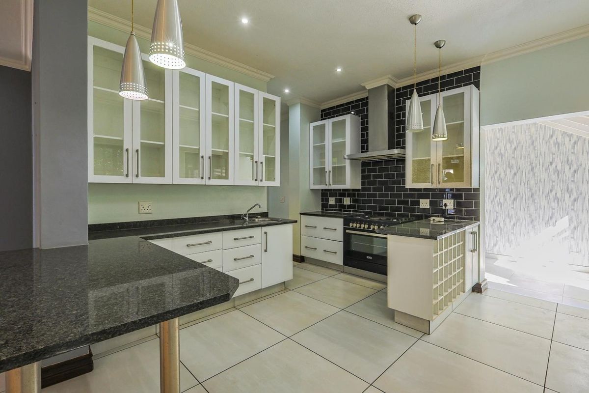 Modern kitchen featuring white cabinetry, dark granite countertops, black subway tile backsplash, stainless steel extractor fan, and built-in wine rack.