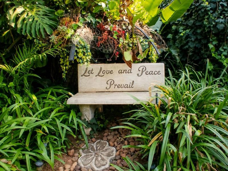 A tranquil garden setting featuring a stone bench nestled among lush greenery and a decorative pebble pathway.