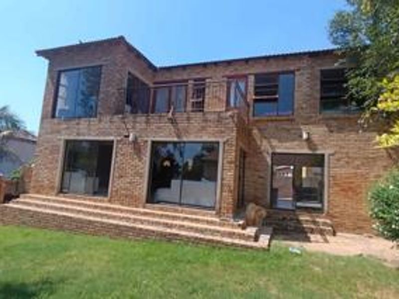 Rear view of a two-story face brick townhouse featuring a ground-level patio with brick steps and an upper-level balcony with metal railings.