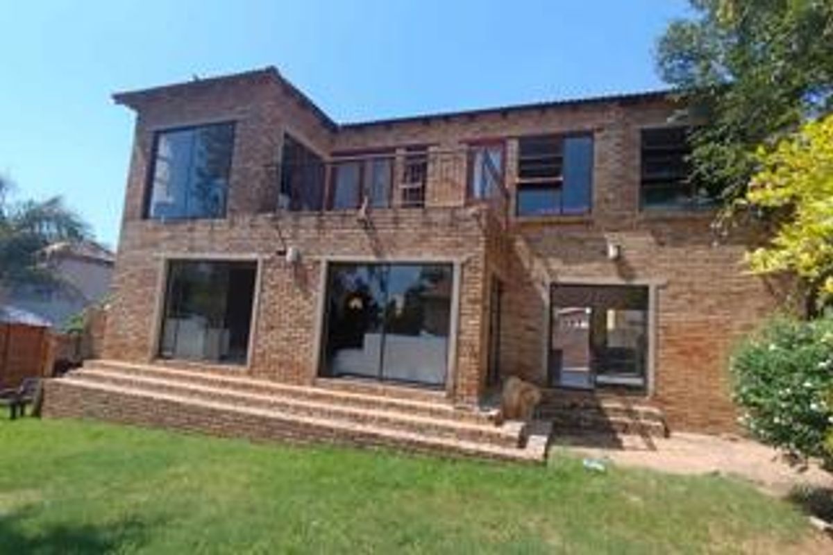 Rear view of a two-story face brick townhouse featuring a ground-level patio with brick steps and an upper-level balcony with metal railings.