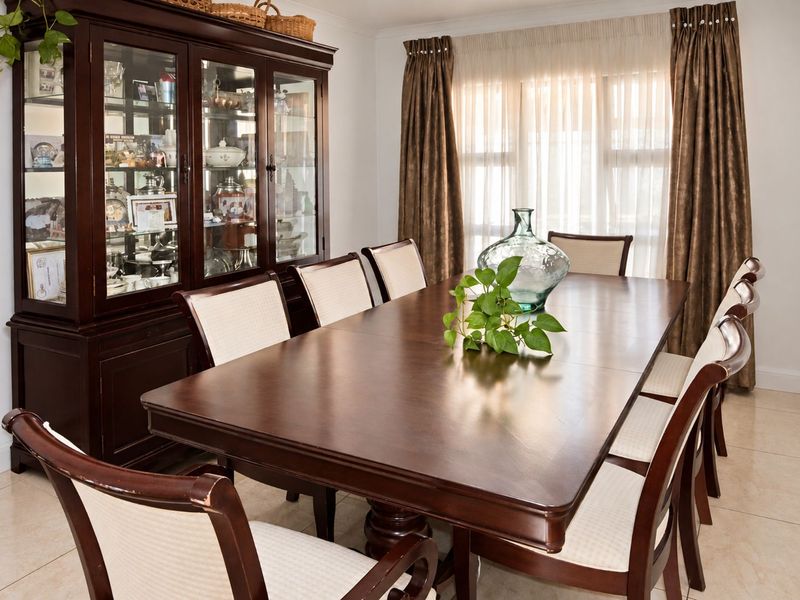 A well-lit dining room featuring neutral tiled flooring and window treatments, providing a functional space for formal meals and gatherings.