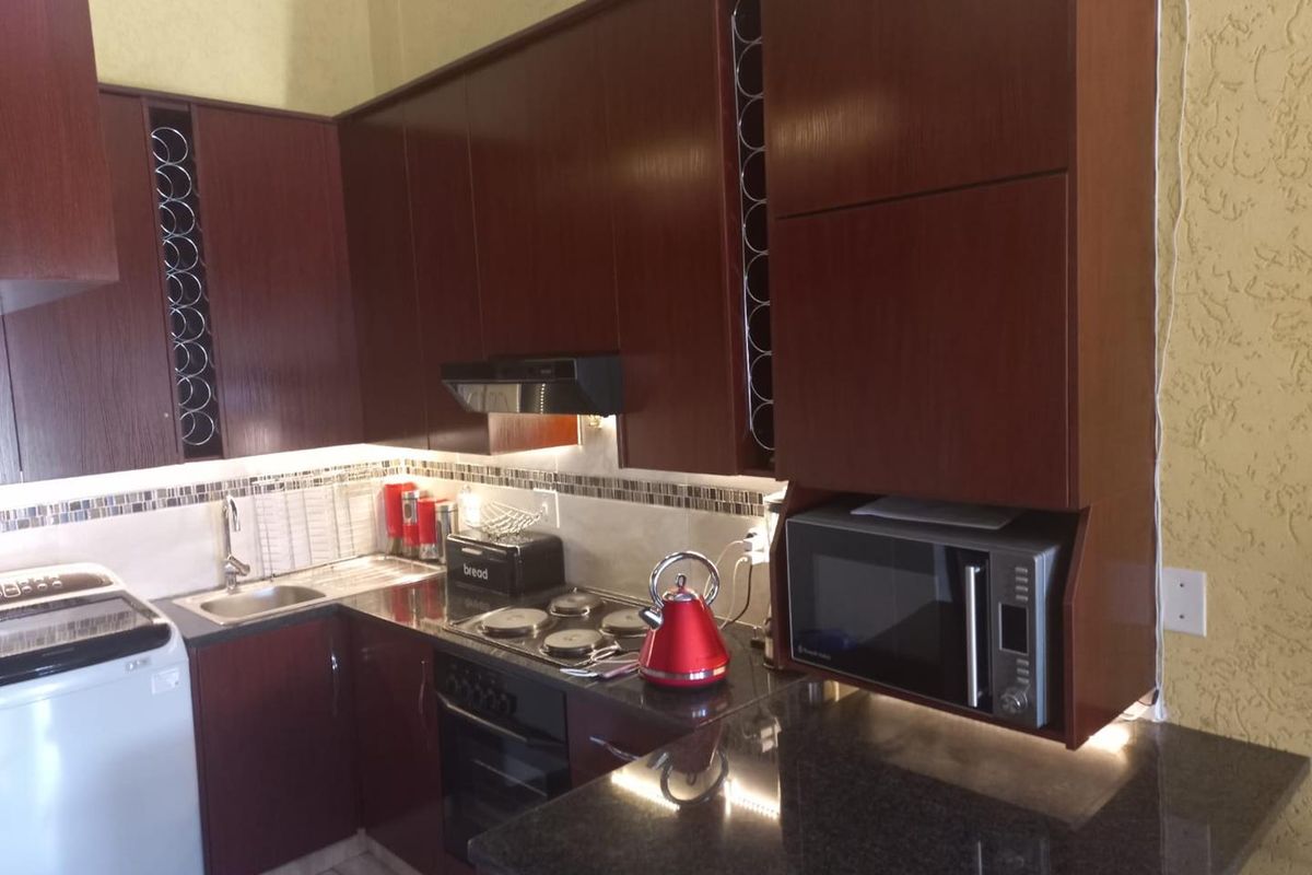 A compact kitchen featuring dark wood cabinetry, granite countertops, a built-in oven, hob, extractor fan, and integrated space for a washing machine.