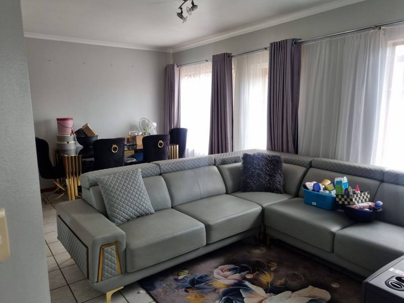 A spacious living area featuring tiled flooring and large windows with installed curtain rails, providing ample natural light.