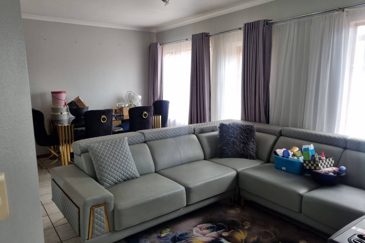 A spacious living area featuring tiled flooring and large windows with installed curtain rails, providing ample natural light.