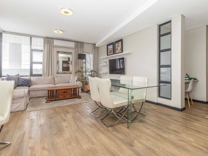Spacious open-plan living and dining area featuring modern laminate flooring, a split-system air conditioner, and a stylish glass panel feature wall.
