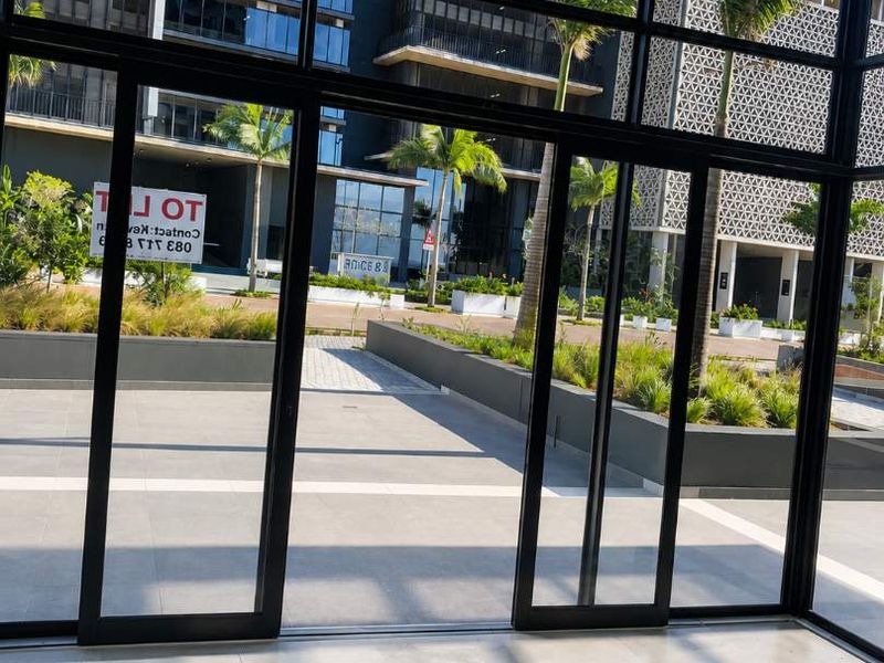 A view from inside looking out through large glass sliding doors onto a modern landscaped courtyard and contemporary building exterior.