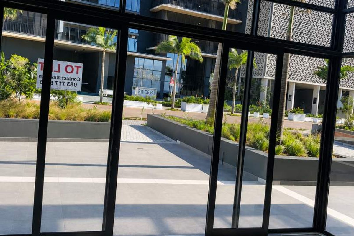 A view from inside looking out through large glass sliding doors onto a modern landscaped courtyard and contemporary building exterior.