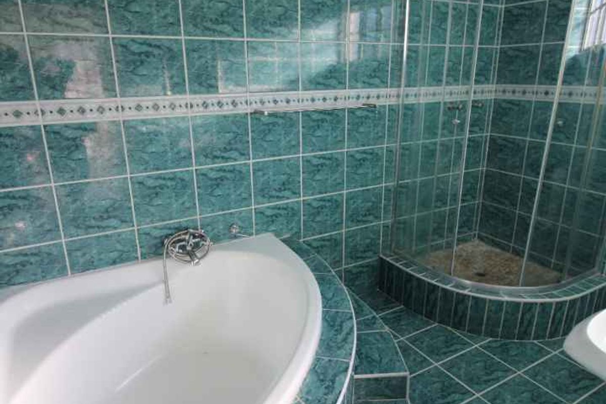 A dated bathroom featuring a corner bathtub and a separate glass-enclosed shower, finished with green marble-effect wall and floor tiles.