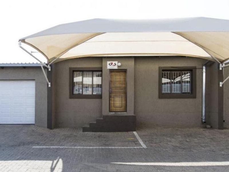 Front exterior view of the townhouse featuring a paved driveway, a covered parking area with a shade sail, and a secure garage entrance.