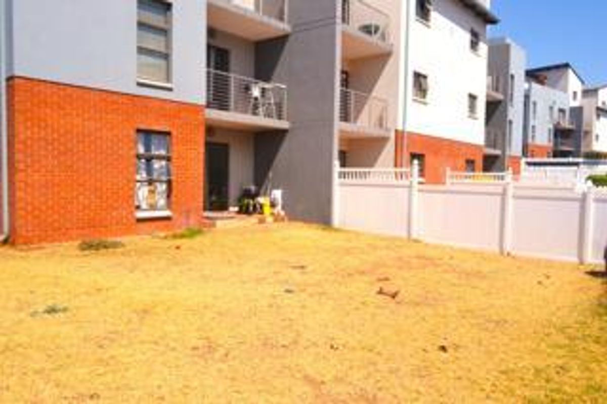 Exterior view of an apartment complex featuring a private ground-floor garden area with brick and plaster facade and balcony access.