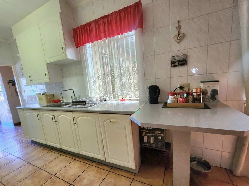 A functional kitchen featuring white built-in cabinetry, laminate countertops, a stainless steel sink, and tiled flooring with a tiled backsplash.