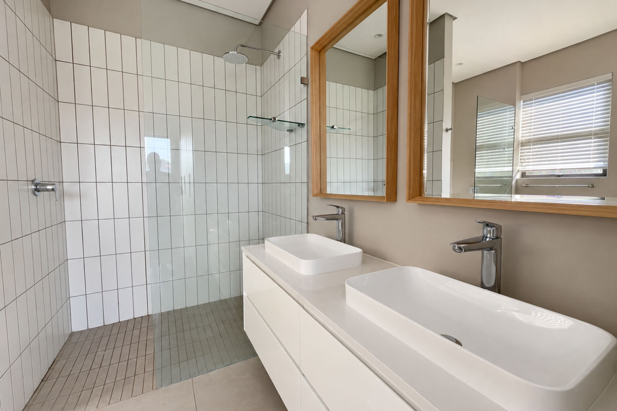 Modern bathroom featuring a double vanity with vessel sinks, chrome fixtures, and a spacious walk-in shower with a glass screen and rain shower head.