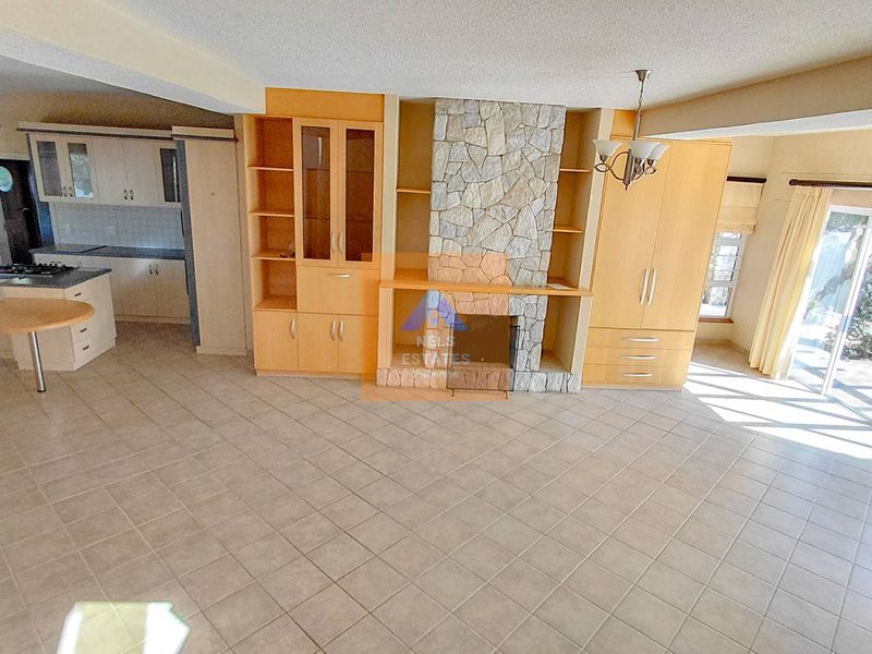 Spacious open-plan living area featuring a stone fireplace, built-in cabinetry, and an adjoining kitchen with tiled flooring and direct access to the patio.