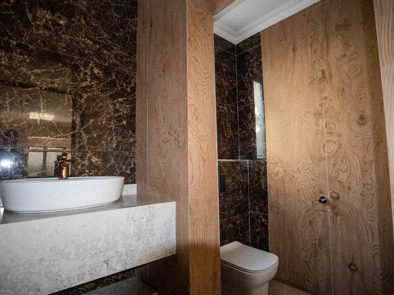 Modern bathroom featuring a vessel sink on a stone vanity, wall-mounted toilet, and a sophisticated combination of dark marble and wood veneer wall paneling.