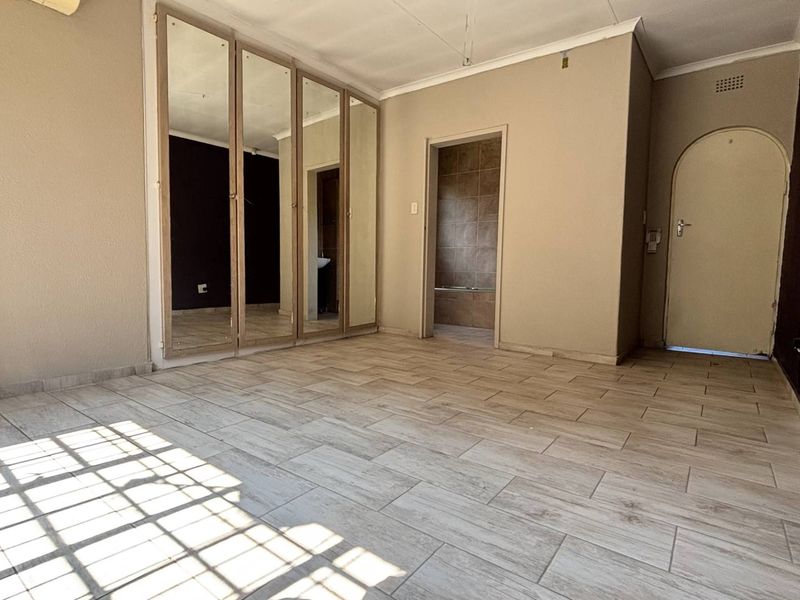 An empty bedroom featuring tiled flooring, built-in mirrored cupboards, and an arched doorway leading to an adjacent room.