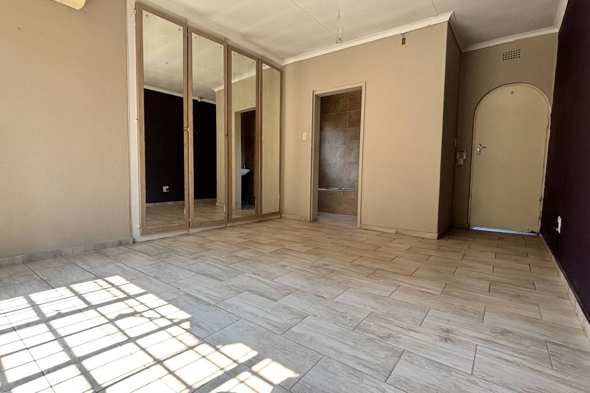 An empty bedroom featuring tiled flooring, built-in mirrored cupboards, and an arched doorway leading to an adjacent room.
