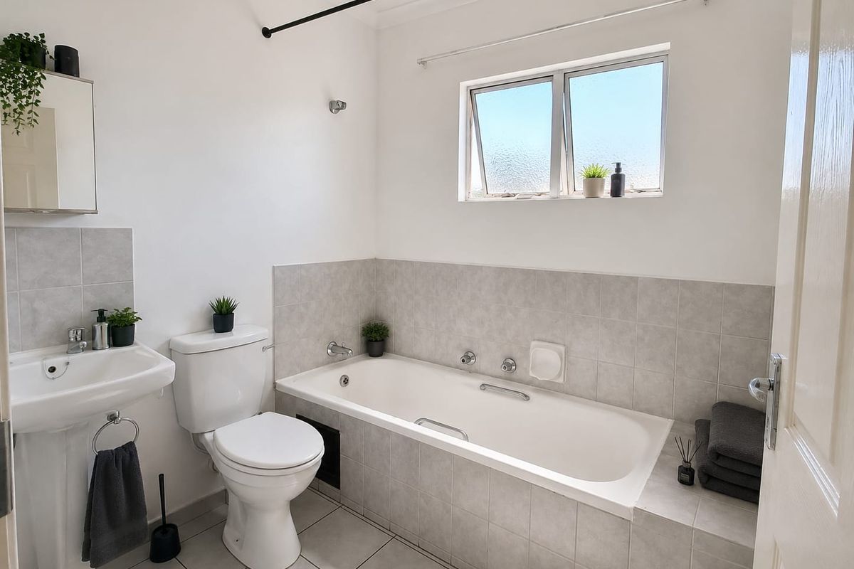 A clean, functional bathroom featuring a pedestal basin, toilet, and a built-in bathtub with tiled surround and splashback.