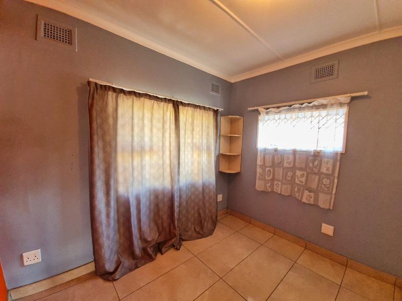 A vacant bedroom featuring tiled flooring, built-in corner shelving, and security bars on the windows, offering a blank canvas for potential updates.