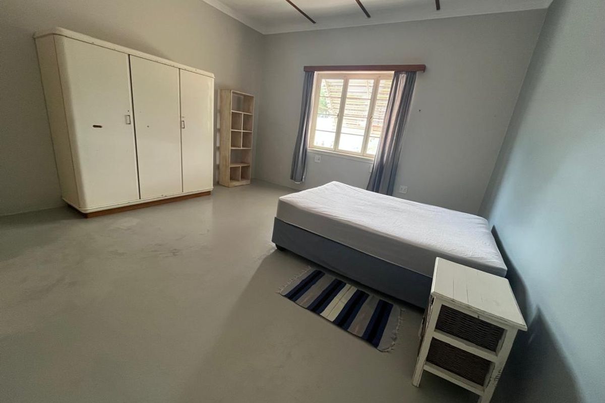 A spacious bedroom featuring painted concrete flooring and exposed timber ceiling beams, offering a neutral canvas for potential interior updates.