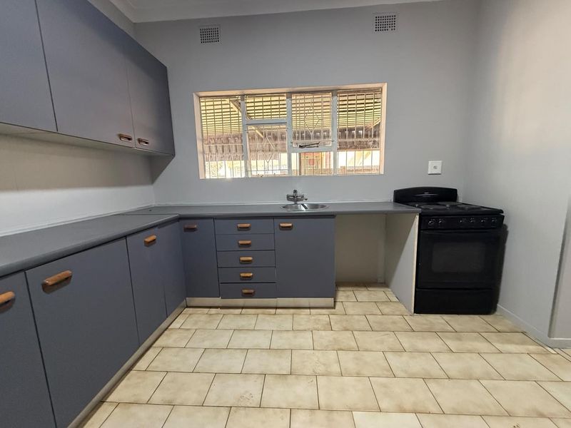 A functional kitchen featuring grey built-in cabinetry, laminate countertops, a stainless steel sink, and a freestanding stove with tiled flooring.