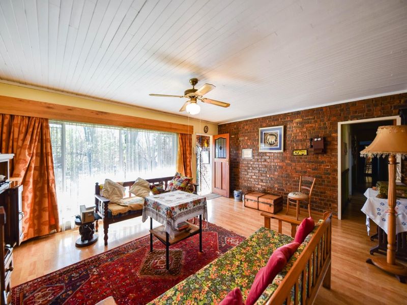 Spacious living room featuring an exposed brick feature wall, timber ceiling with fan, and large windows providing ample natural light.