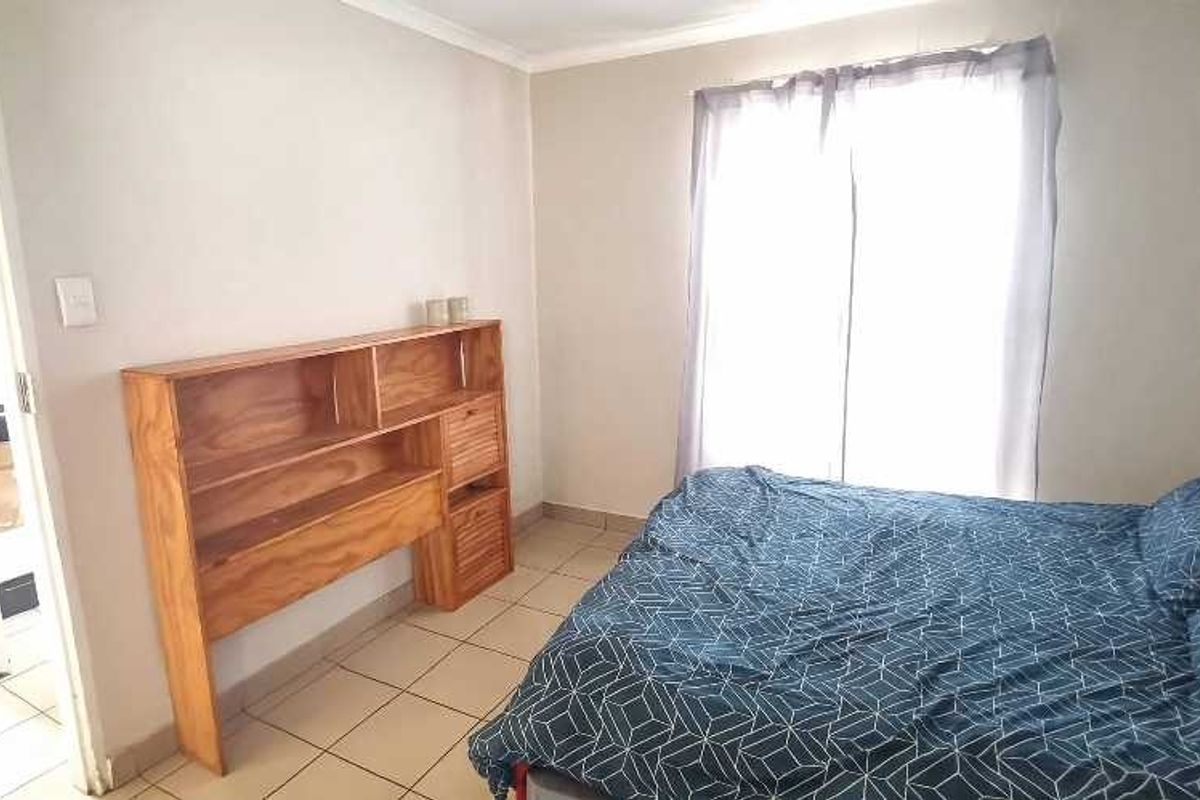 A functional bedroom featuring tiled flooring, a built-in wooden shelving unit, and a sliding door providing natural light.