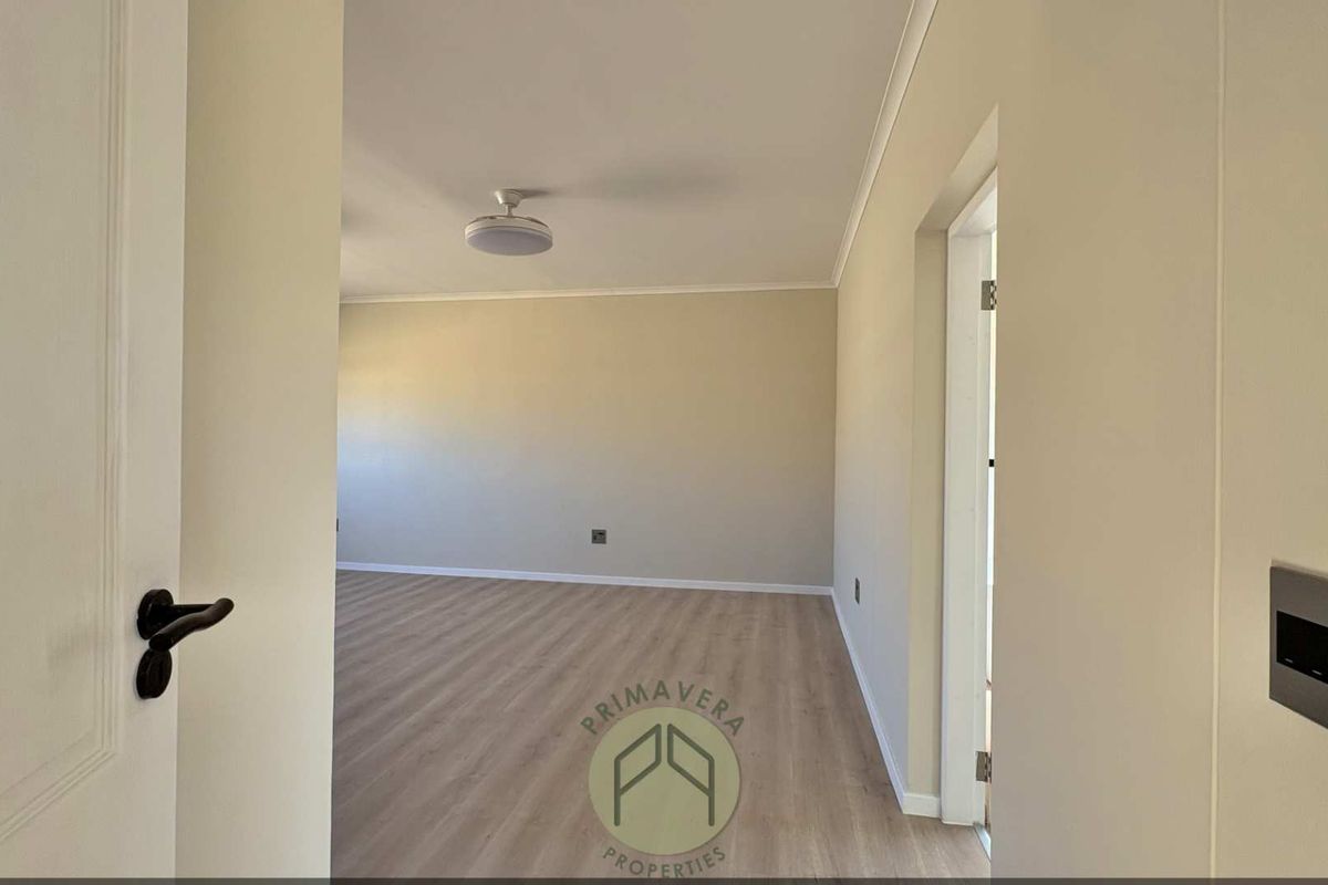 A bright, neutral-toned living area featuring modern wood-look flooring, recessed ceiling lighting, and clean, minimalist finishes.