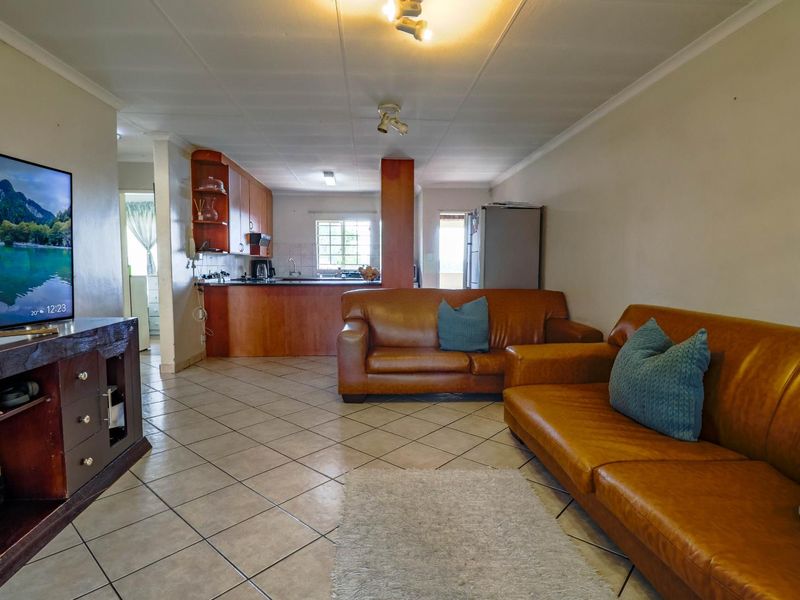 Open plan living area featuring tiled flooring and a functional kitchen with built-in cabinetry and sink, creating a combined living and dining space.