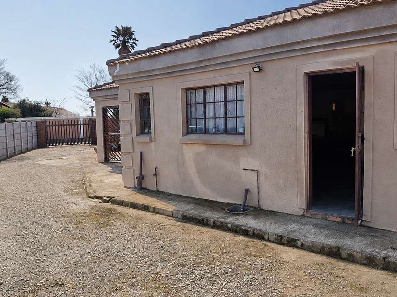 Rear view of the property featuring a plastered exterior, tiled roof, security-barred windows, and a large gravel and concrete driveway area.