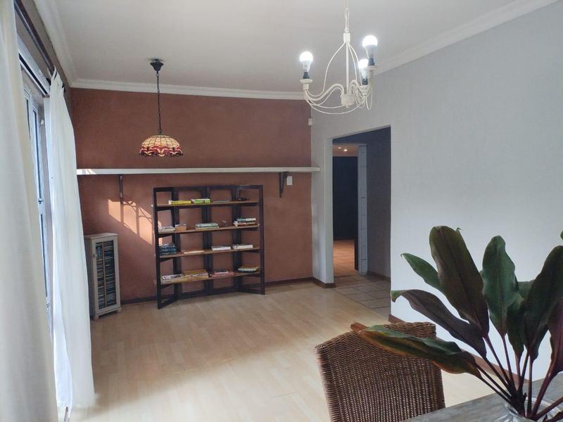 A living room featuring laminate flooring, a decorative pendant light, and a wall-mounted shelf, with a neutral color scheme and coving details.