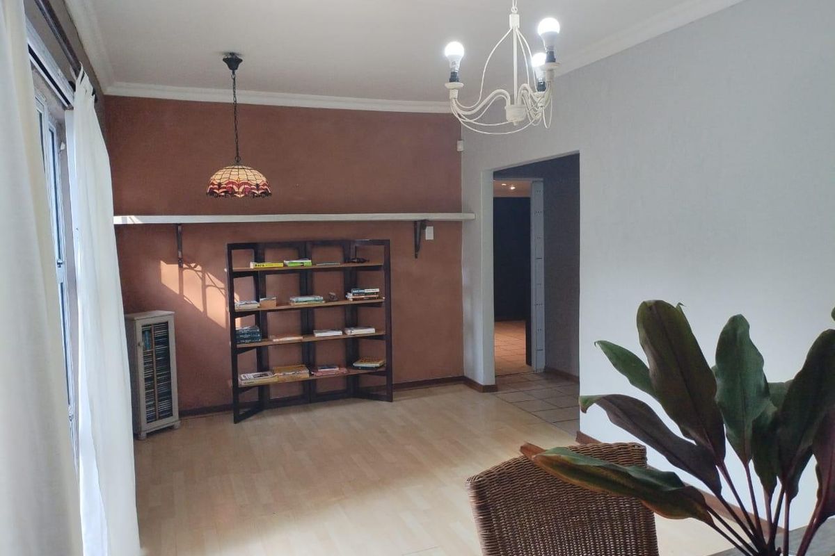 A living room featuring laminate flooring, a decorative pendant light, and a wall-mounted shelf, with a neutral color scheme and coving details.