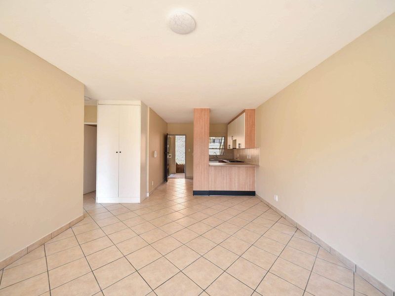 An open-plan living and kitchen area featuring tiled flooring, built-in storage cupboards, and a functional kitchen layout with cabinetry.