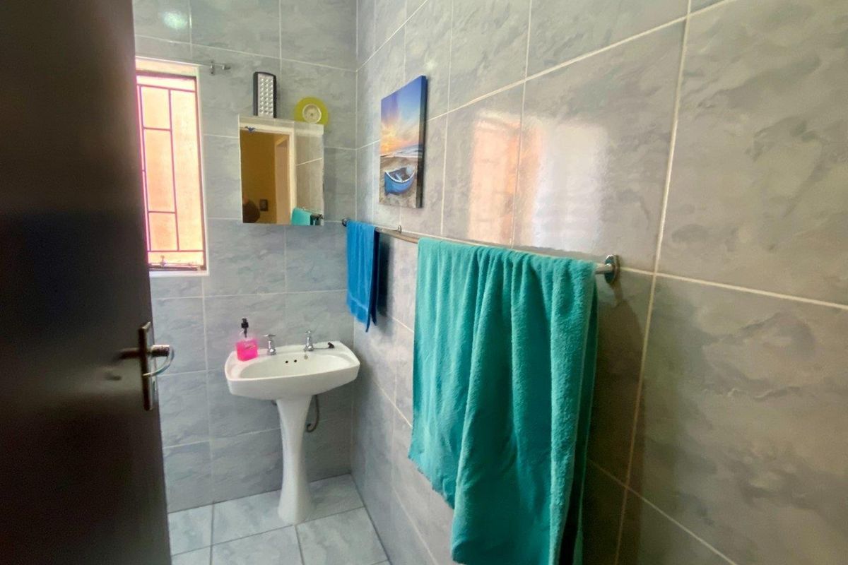 A functional bathroom featuring full-height wall tiling, a pedestal basin, and a window with security bars.