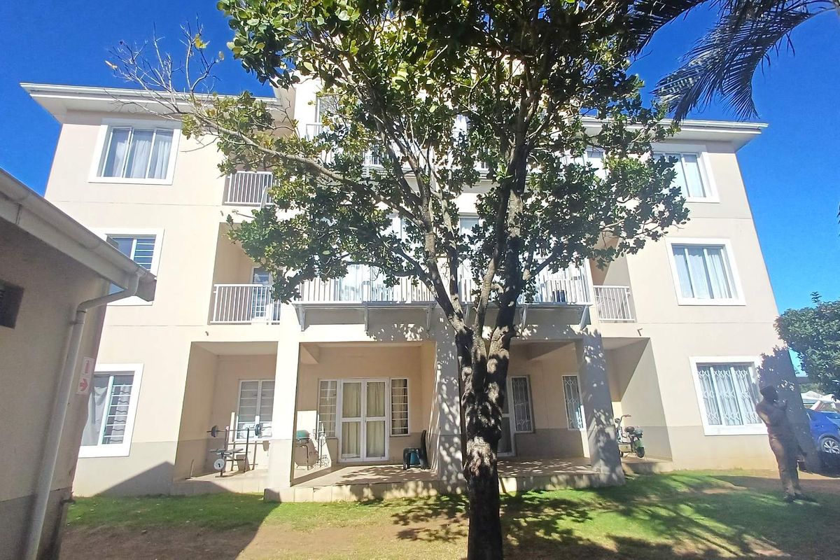 Rear elevation of a multi-story apartment building featuring balconies, security bars on windows, and a ground-level paved patio area.