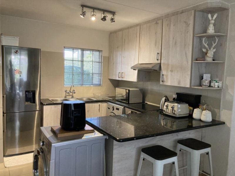 A functional kitchen featuring light wood-grain cabinetry, dark granite countertops, a double sink, and integrated extractor fan with modern track lighting.