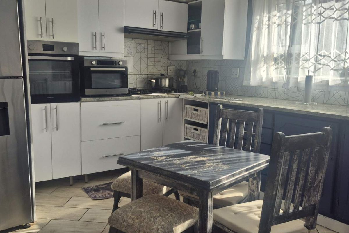 A functional kitchen featuring white and dark cabinetry, stone countertops, built-in oven and microwave, and a tiled backsplash with natural light.