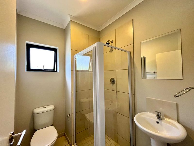 A functional bathroom featuring a shower enclosure, pedestal basin, toilet, and wall mirror, finished with neutral wall tiles and paint.