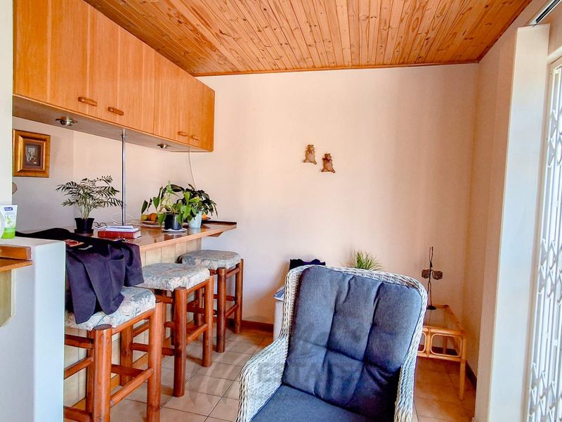 A compact kitchen area featuring a breakfast bar, overhead timber cabinetry, and a timber-paneled ceiling, leading to a secure exterior entrance.