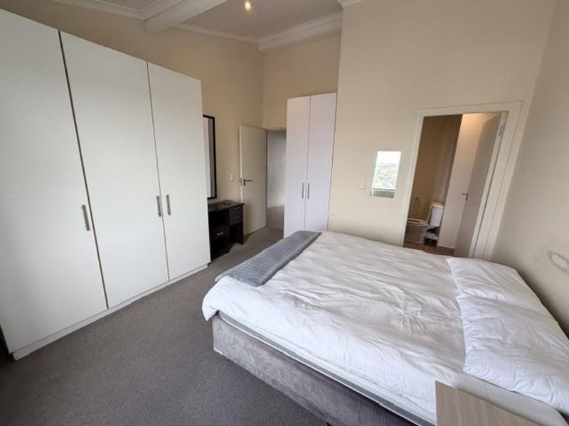 Spacious bedroom featuring extensive built-in cupboard storage, neutral wall finishes, carpeted flooring, and direct access to an en-suite bathroom.