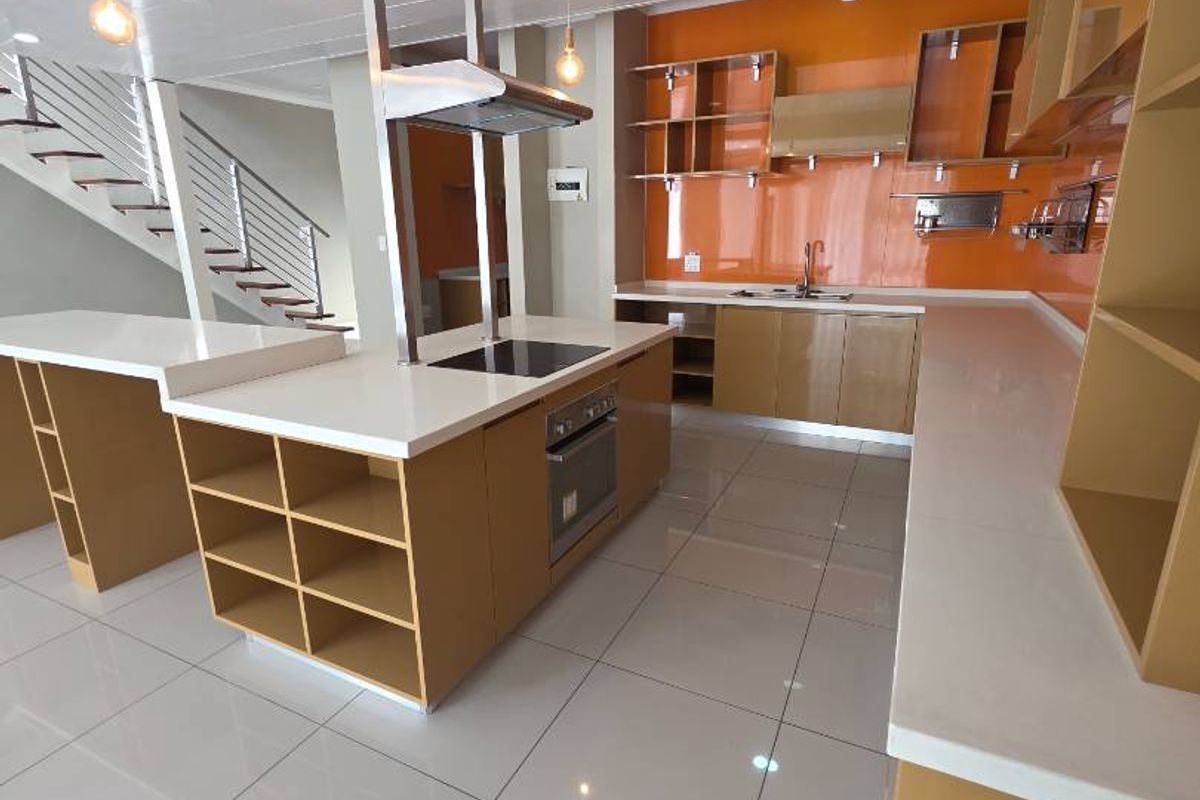 Modern kitchen featuring a central island, built-in oven, electric hob, extractor fan, and sleek cabinetry with orange glass splashbacks and tiled flooring.