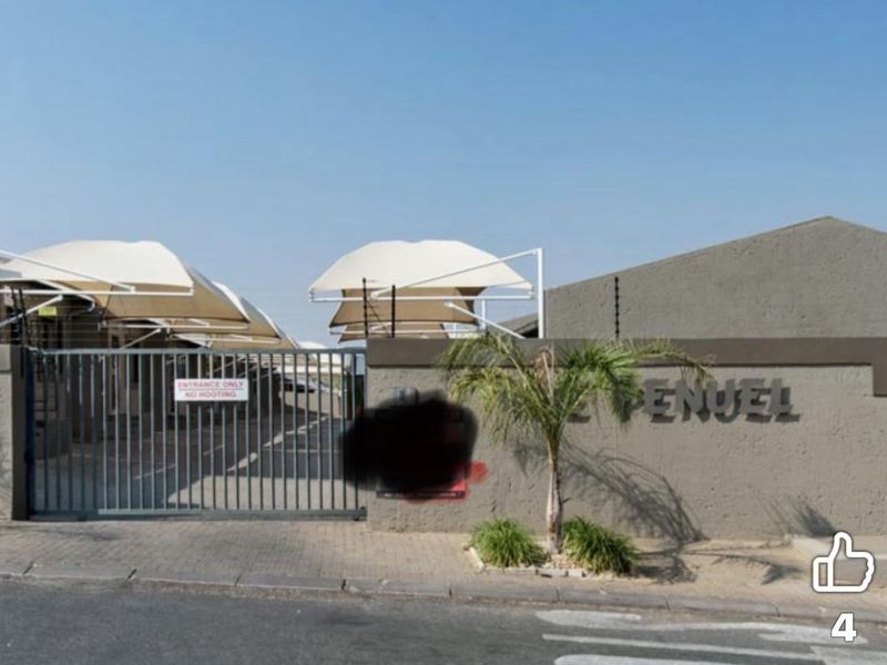 Front entrance view of the townhouse complex featuring a secure metal gate, electric fencing, and covered parking bays.