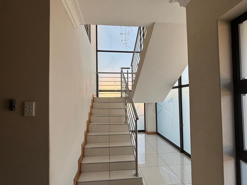 A bright and modern entrance hallway featuring a tiled staircase with a metal balustrade and large windows that allow for ample natural light.