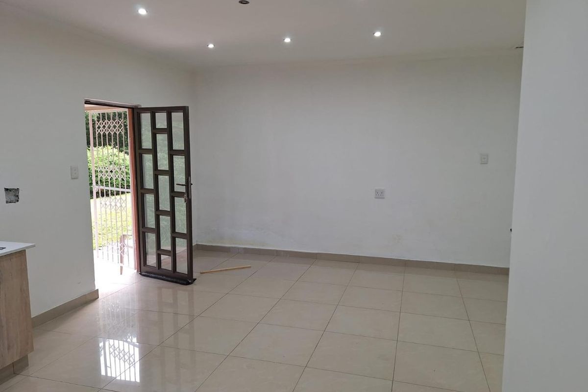 An empty open-plan living area featuring tiled flooring, recessed downlights, and direct access to an outdoor space through a security gate.