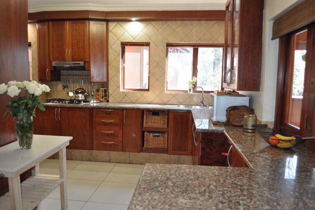 A functional kitchen featuring warm-toned wooden cabinetry, granite countertops, a gas hob with extractor fan, and tiled backsplash with ample natural light.