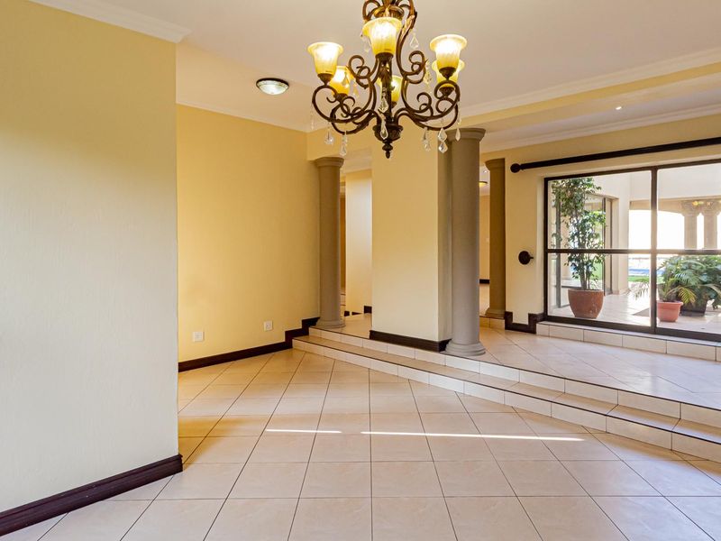 Spacious living area featuring tiled flooring, decorative columns, a chandelier, and large sliding glass doors providing access to the outdoor patio area.