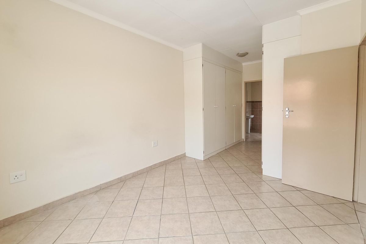 An empty bedroom featuring neutral tiled flooring and built-in cupboards, offering a clean and versatile space ready for personalization.