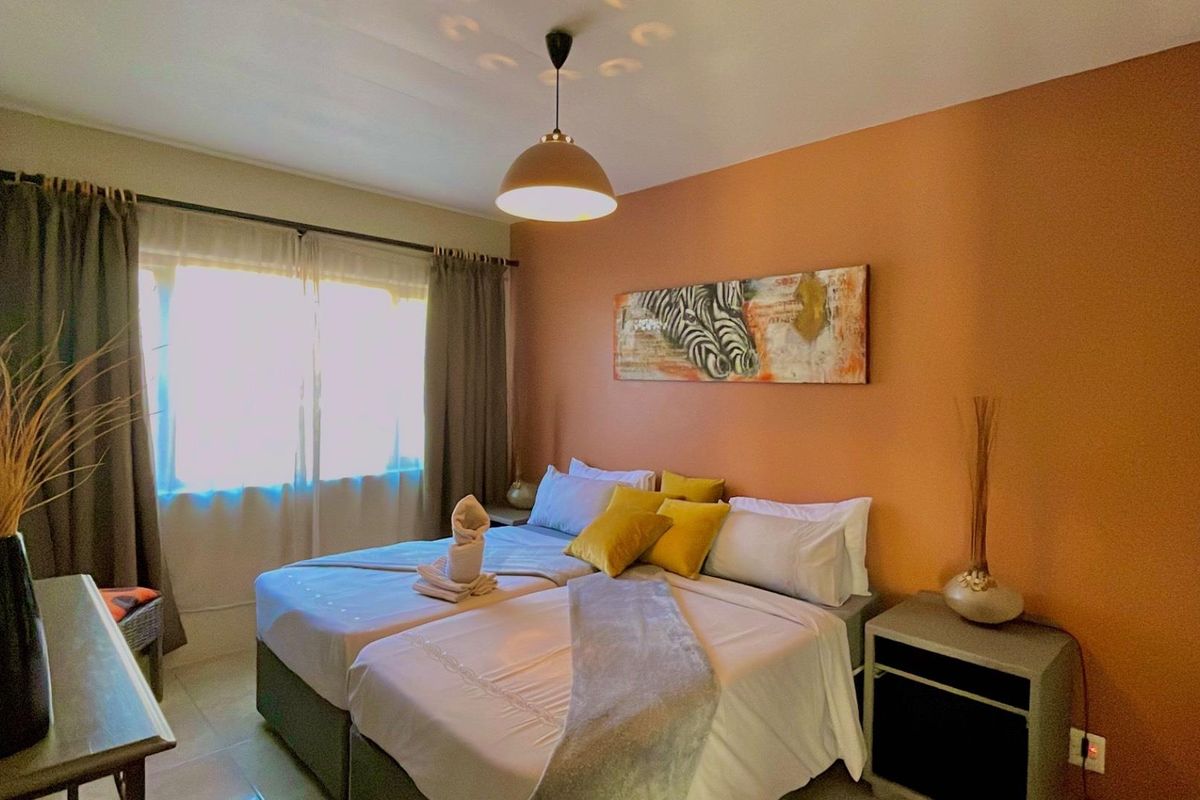A well-lit bedroom featuring a warm-toned accent wall, tiled flooring, and a central pendant light fixture.