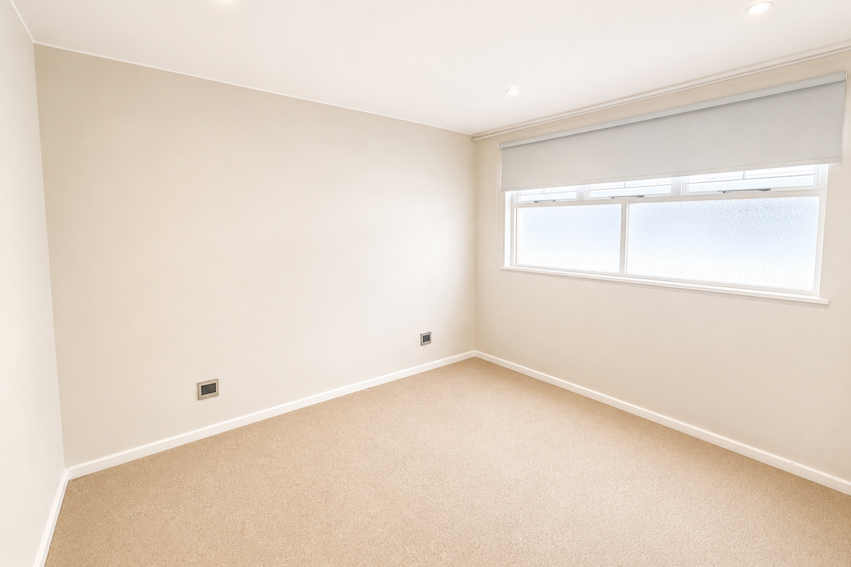 A clean, neutral-toned bedroom featuring carpet flooring, recessed downlighting, and a fitted roller blind over the window.